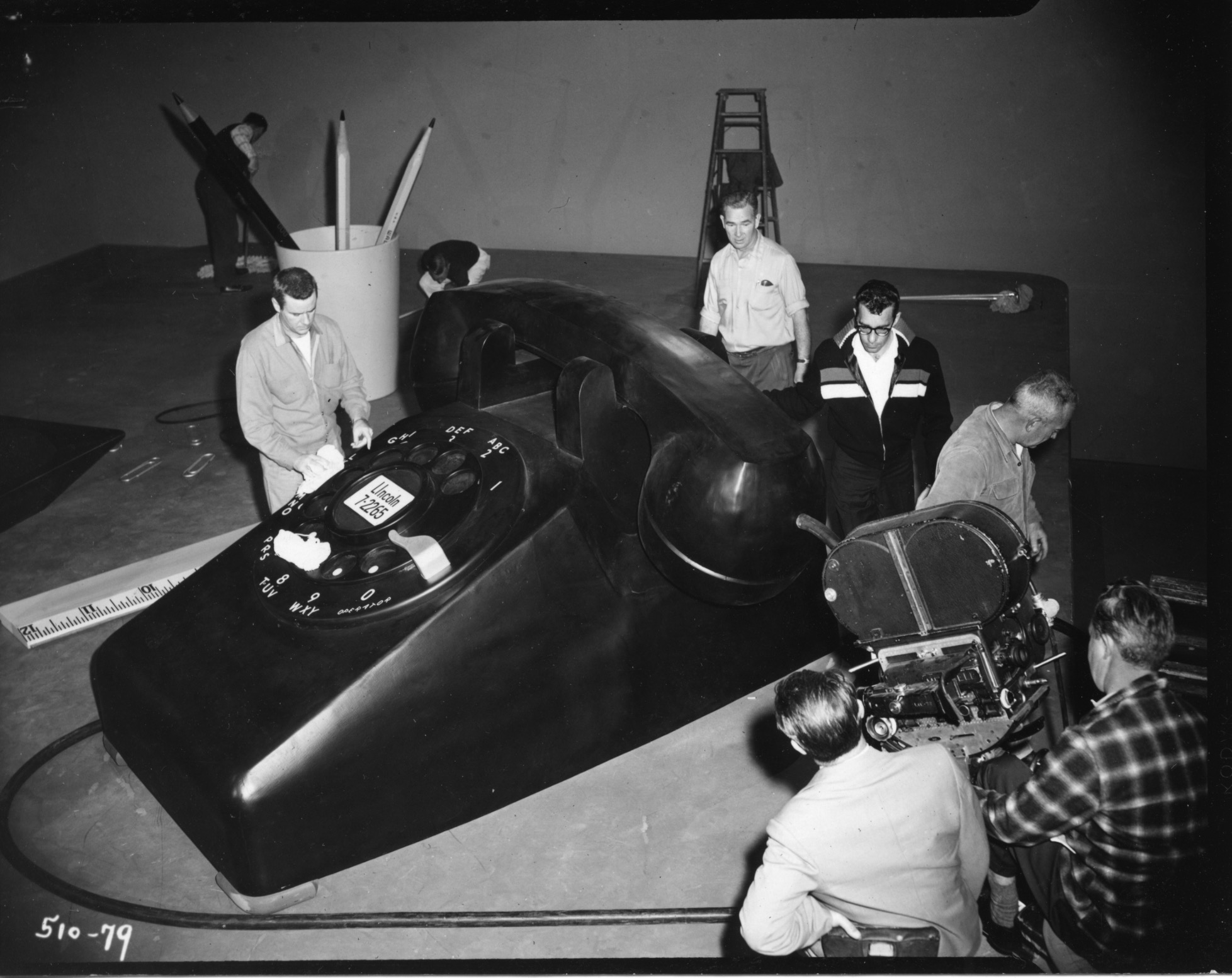 production crew members work on a huge rotary phone set piece